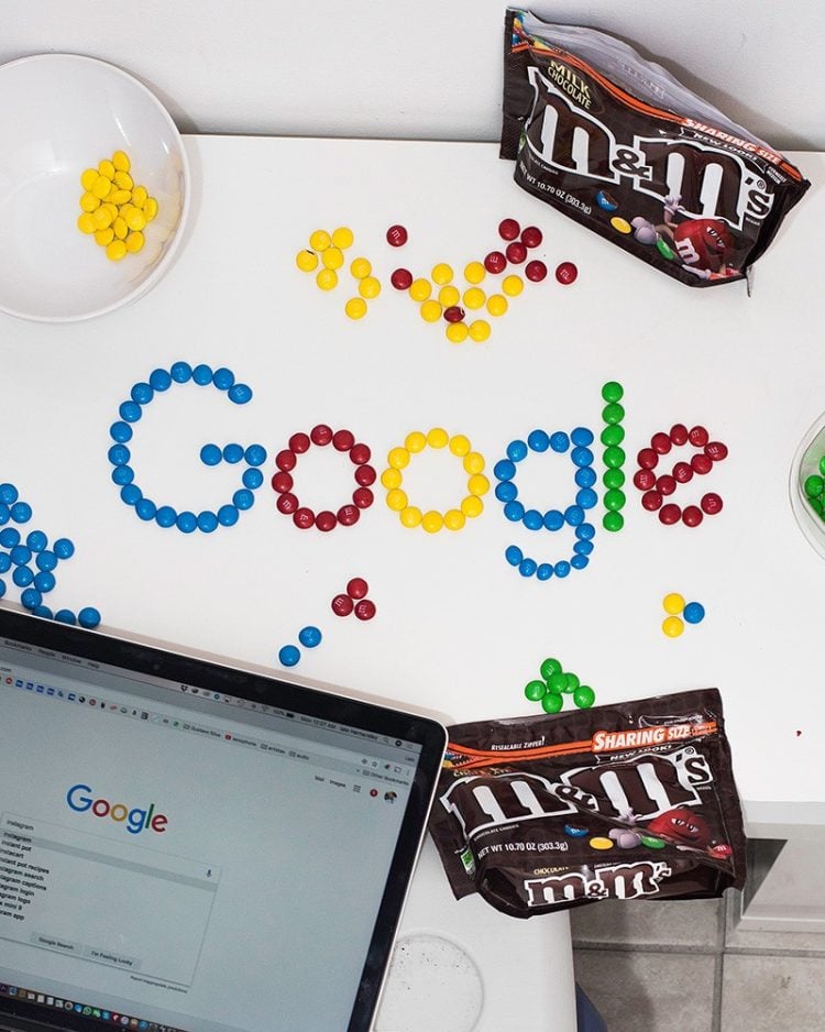 m&ms on table arranged to spell google on white table with laptop that has google search on screen