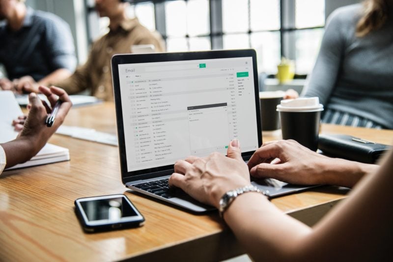 person typing on laptop sitting at a wood table having a meeting