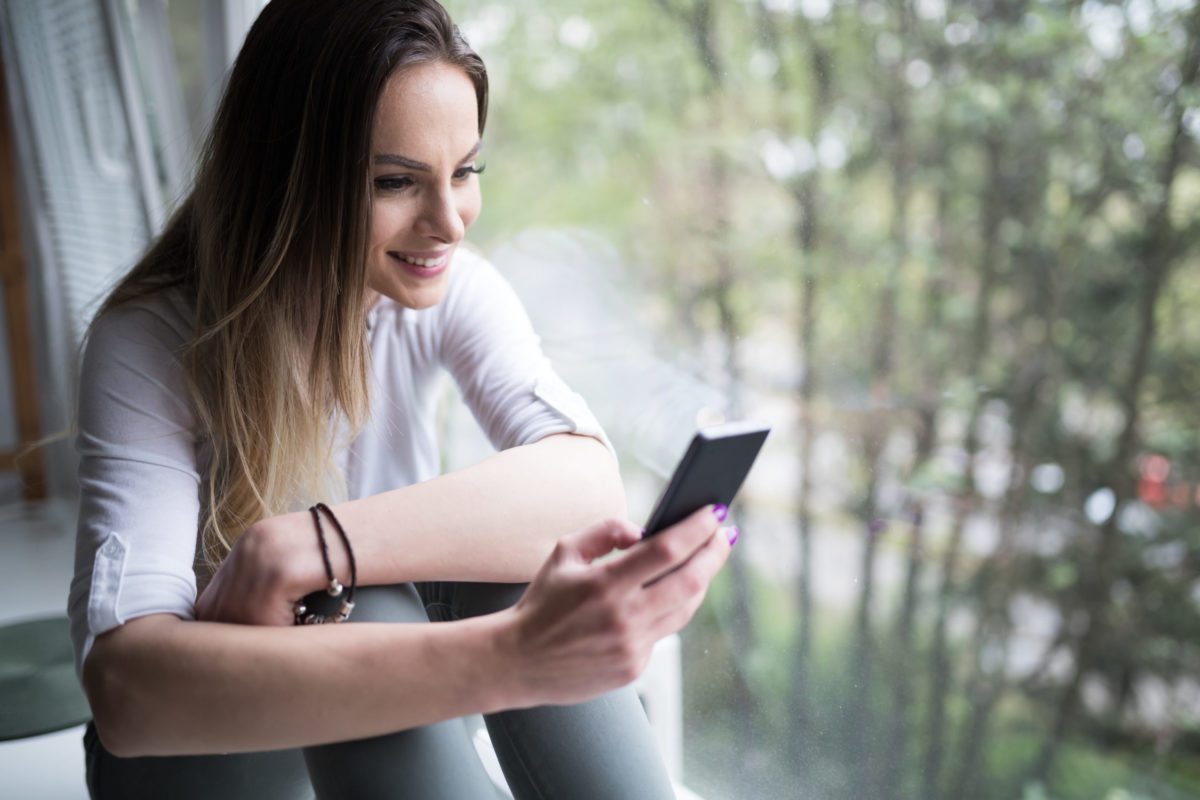 Woman using cell phone at home to connect to social media network
