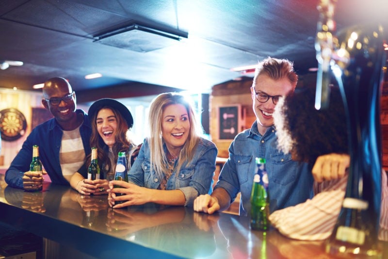 group of happy people drinking bottles of beer at a bar