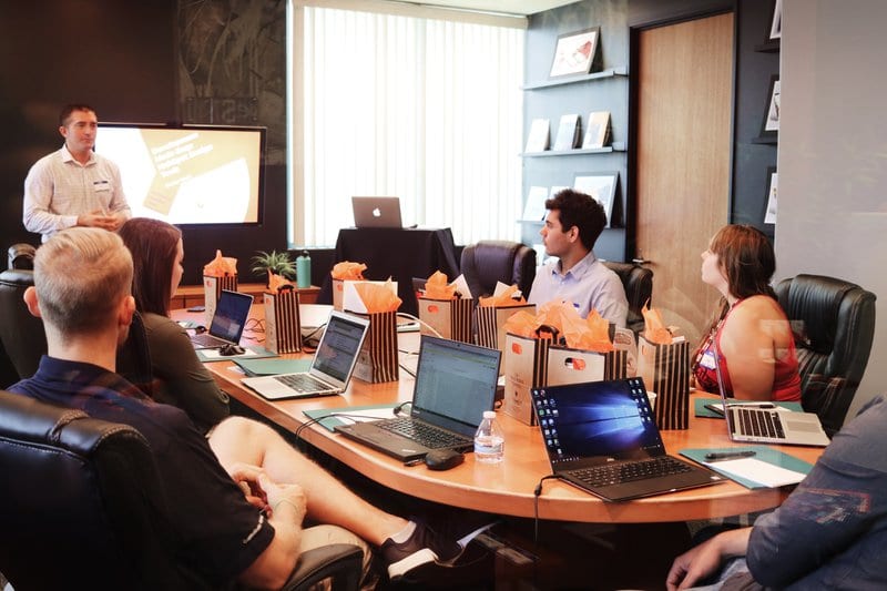 people seated in a board room with laptops on the shared table, they are all watching a presentation about on-page seo