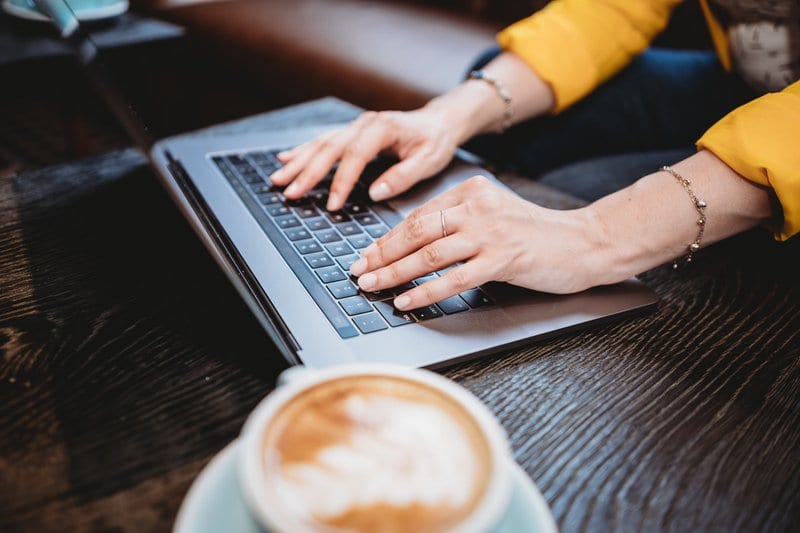 Digital marketing freelance working on a computer at a wooden table with a cup of coffee.
