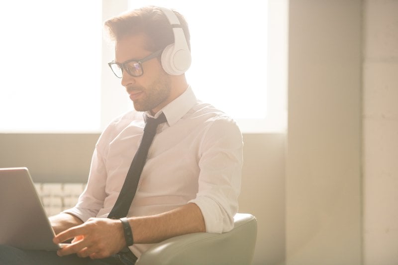 Concentrated young SEO expert with stubble sitting in armchair and using laptop while taking statistics from websites