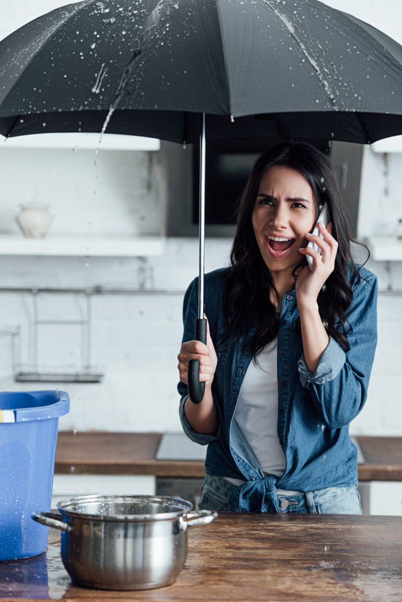 stressed-woman-using umbrella during leak in kitchen
